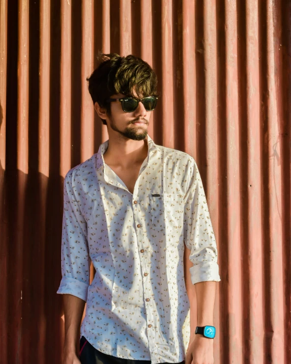 young man wearing sunglasses and white shirt near corrugated wall