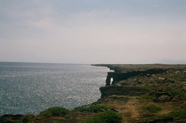 a cliff outcropping into the ocean by a tall rock