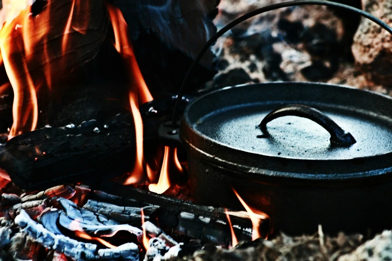 a camp stove sitting next to a pile of logs and a pot