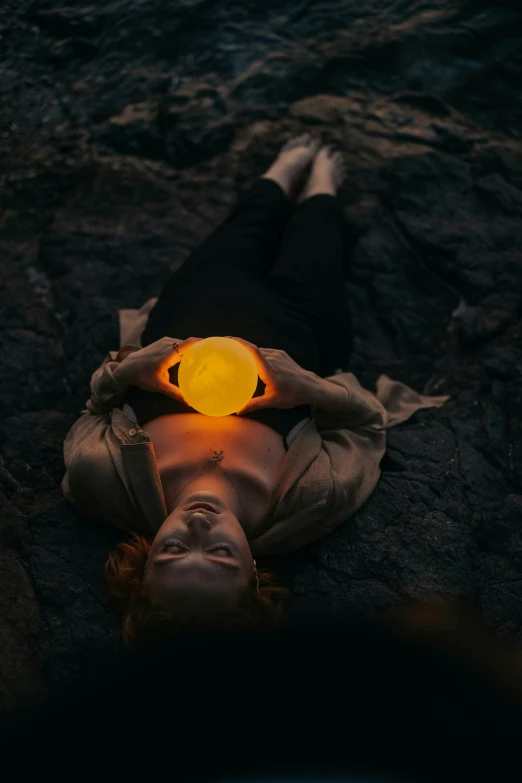 a woman with orange glowing ball laying on the ground