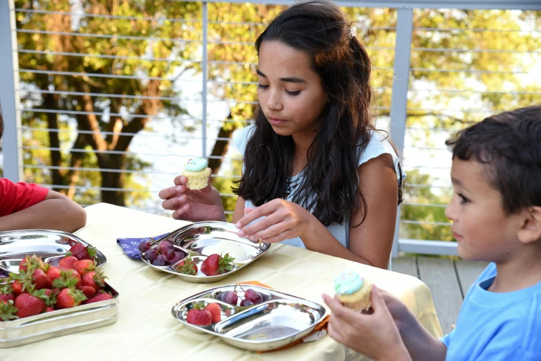 three children sitting at a table eating food