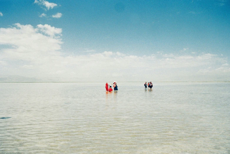 a group of people standing in the ocean on top of a calm day