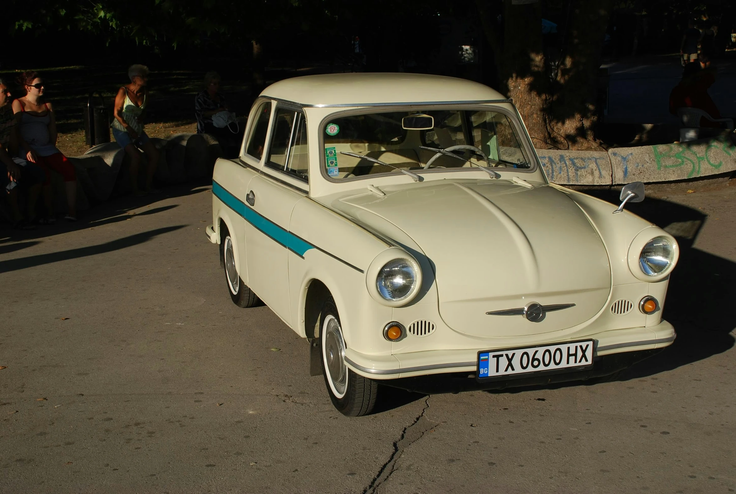 the vintage white car is parked along with people