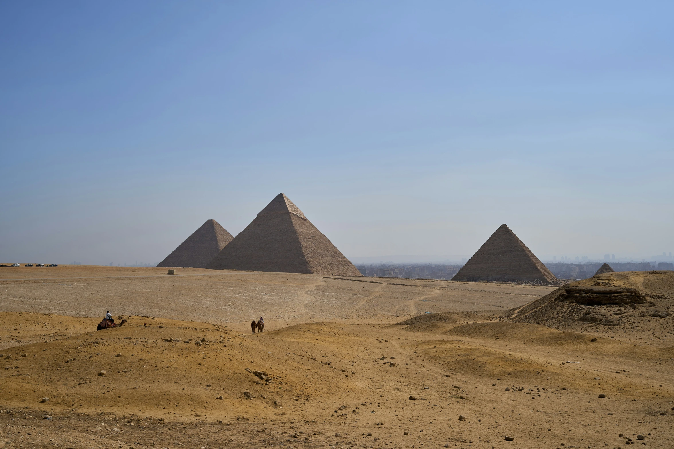 a view of a desert with camels and pyramids