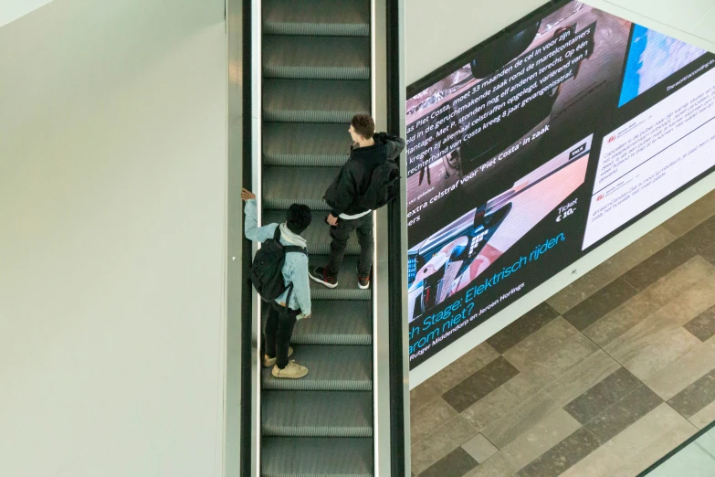 two people riding down a escalator with large banners behind them