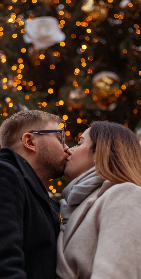 a woman and man standing together outside with a christmas tree