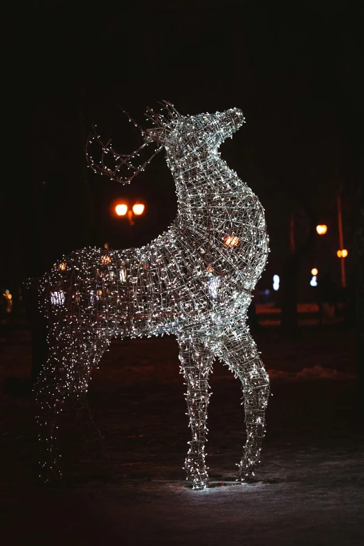 a lighted deer standing in a park during the night