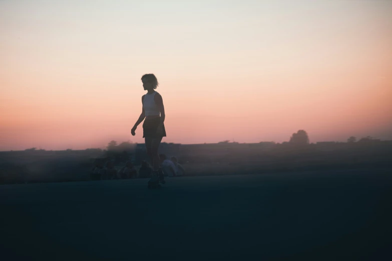 a woman standing with one foot on her skateboard in the sunset