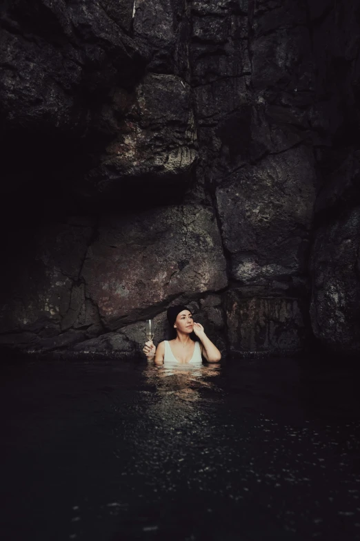 a woman in the water holding a cigarette in front of a rock formation