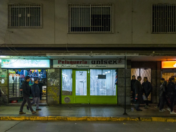 a small green building that has people walking on the street in front