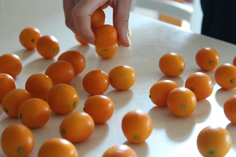 many oranges on a white countertop with one person reaching for one