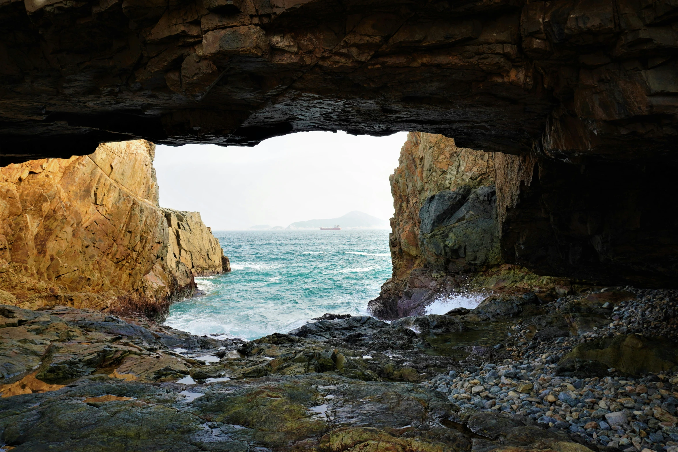 a cave with large rocks and an open doorway overlooking the ocean