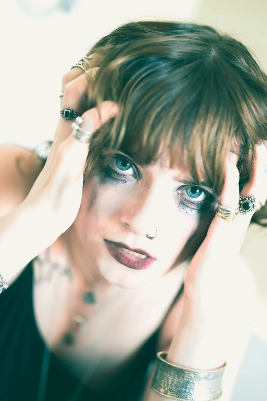 a woman in black with piercings holding her hair up to her face