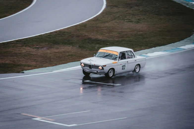 an old race car with orange trim on it's hood drives down a track