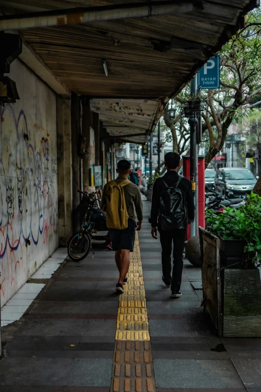 a couple of people walking down the sidewalk next to a graffiti covered wall