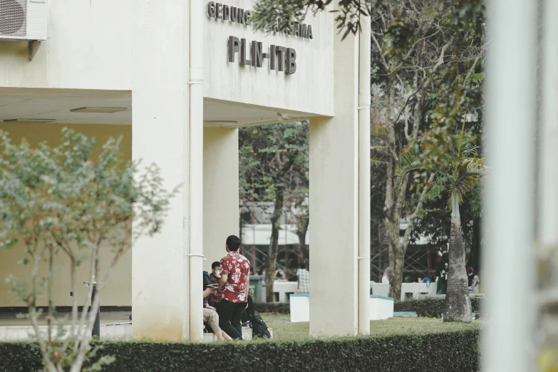 man sitting outside a building near a shrub