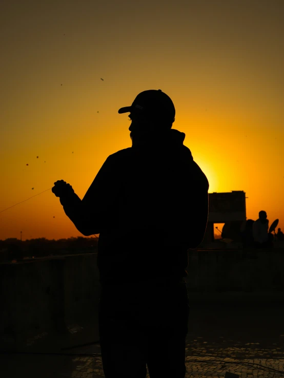 a silhouette of a man holding kites during a sunset