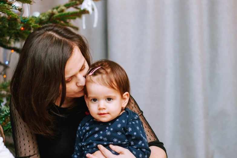 a woman is holding her toddler in front of a christmas tree