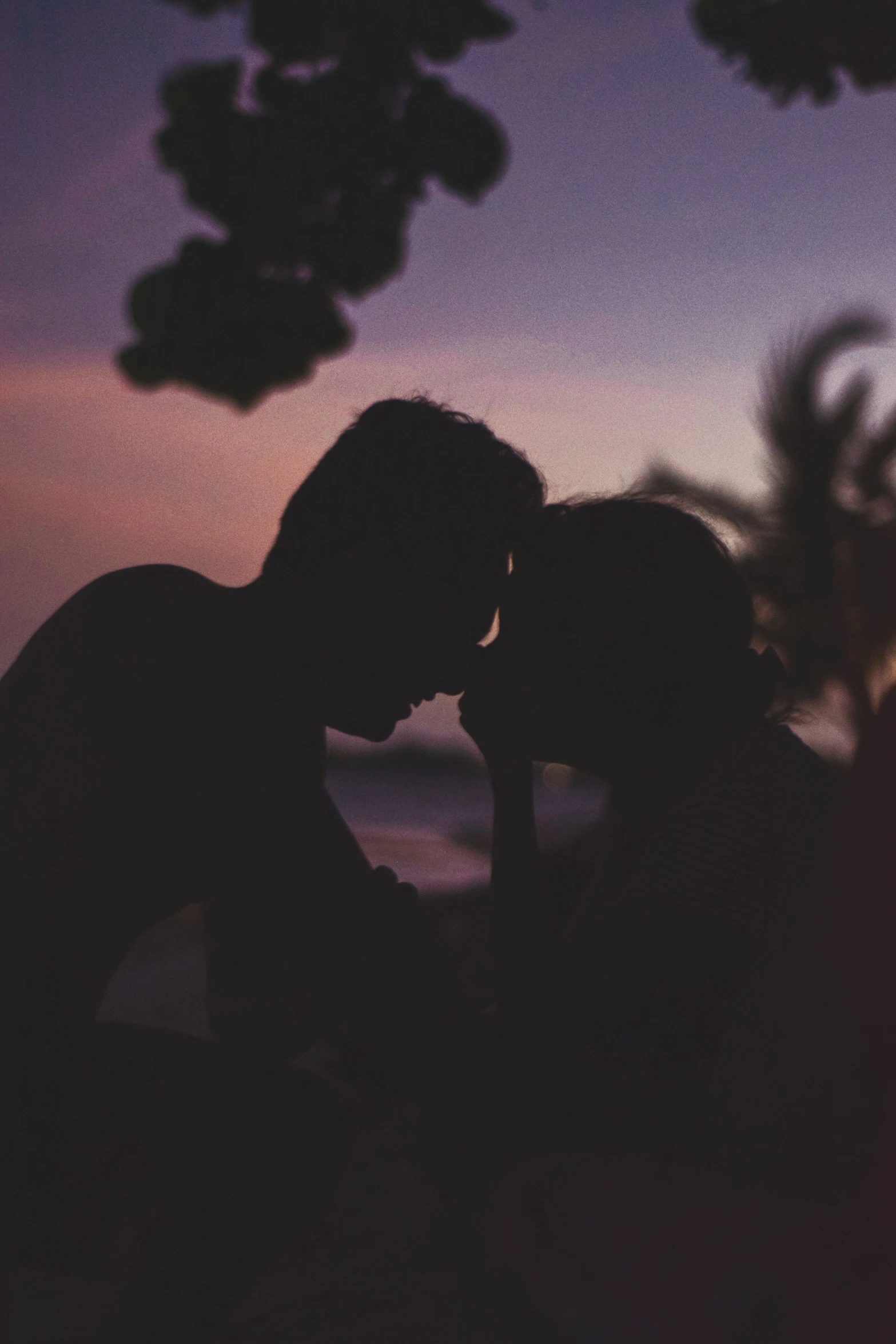 two silhouettes of people kissing over a sunset