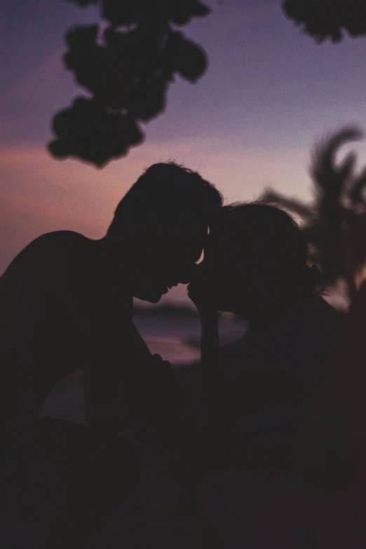 two silhouettes of people kissing over a sunset