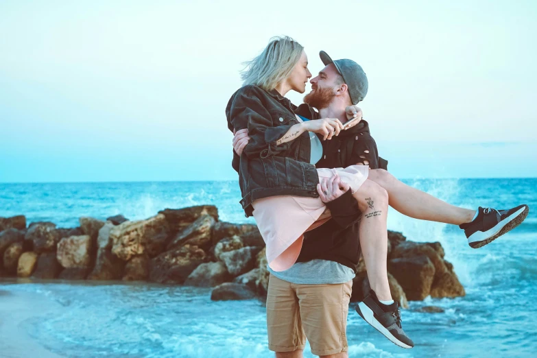 a woman carrying a man on his back while standing next to the ocean