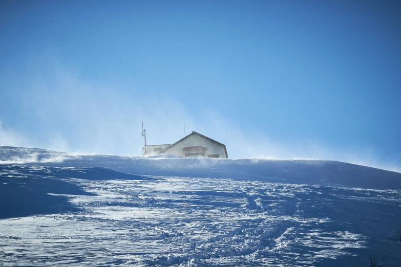 a house on top of a snowy hill in the middle of a blue sky