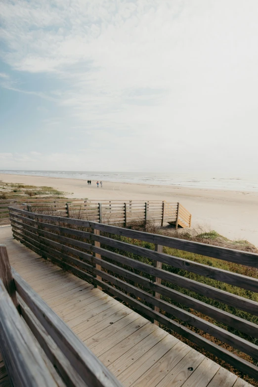 a beach is near a wooden fence and there is a person walking in the background