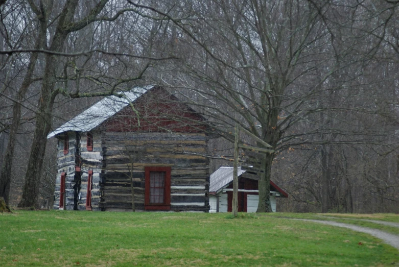 a cabin sits in the middle of a field surrounded by bare trees