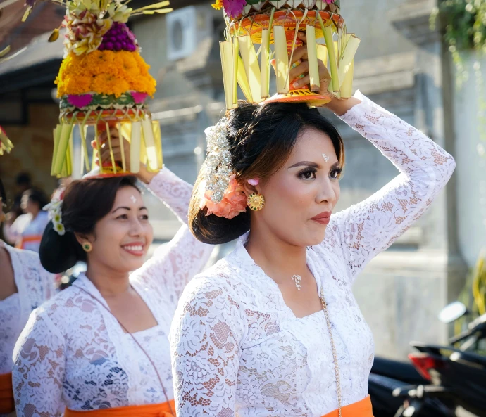 two women in white dresses holding flowers and a basket on their heads