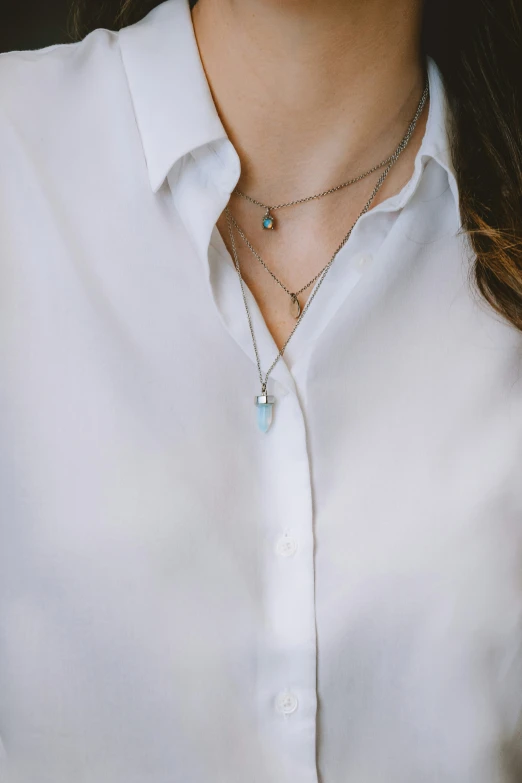 a woman wearing a white shirt and blue glass pendant on her neck