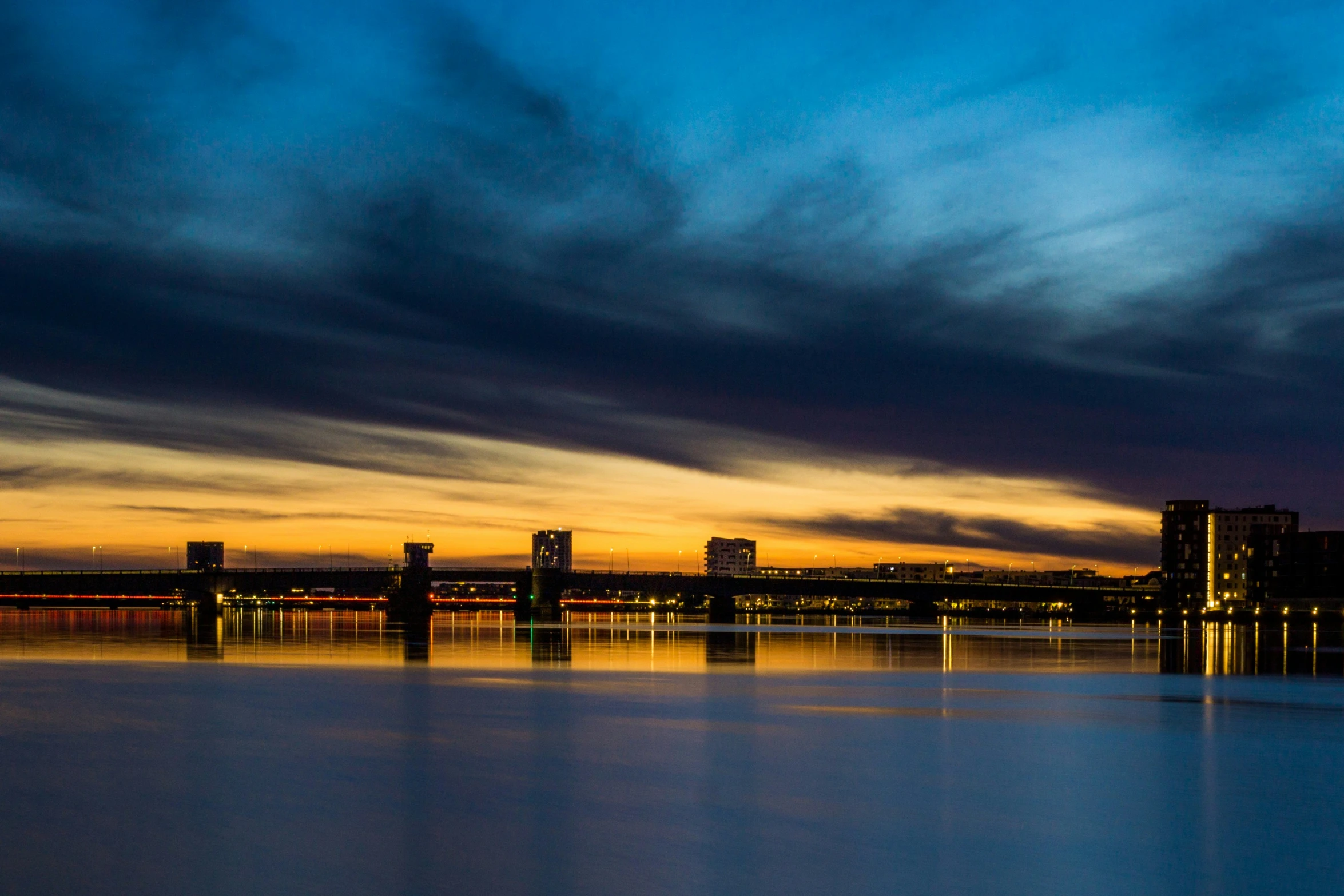 water reflecting a skyline at sunset, with a blue sky and white clouds