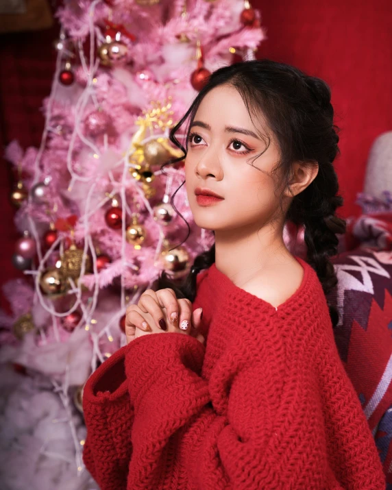 a young woman sitting by a decorated pink tree in a sweater