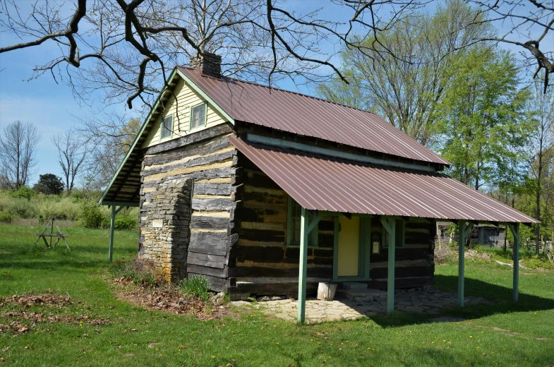 an old log building sitting on top of a grass covered field