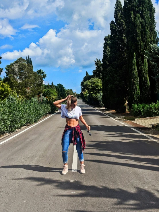 a woman standing next to a road with trees lining the sides