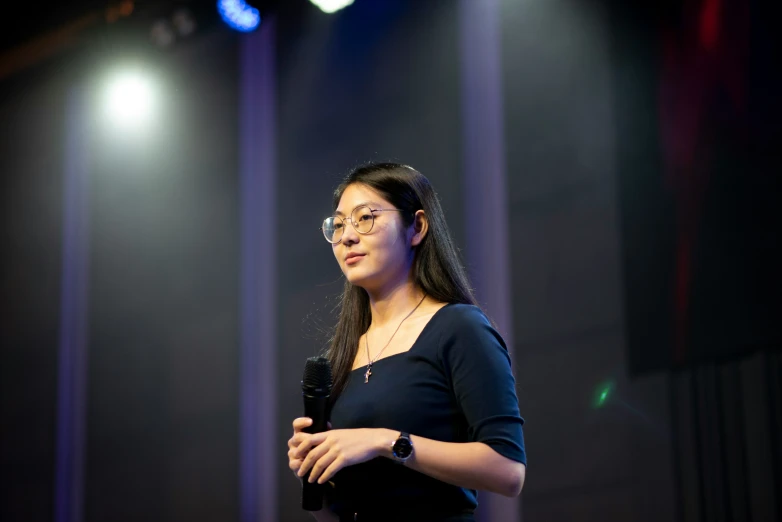 a woman in glasses speaks on stage at an event