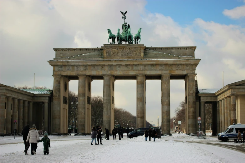 people walk past the large gateway of an older city