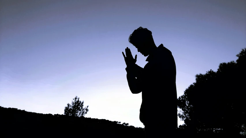 a silhouette of a man clapping in front of a sky