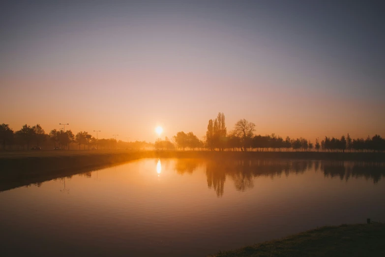 the sun sets behind a lake in the distance