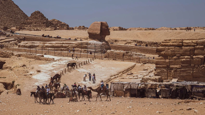 group of people riding camels near egyptian ruins