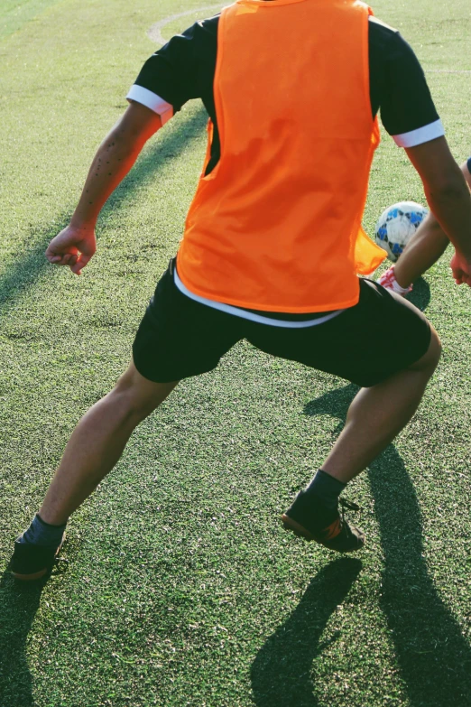 a person in an orange vest and shorts kicking a soccer ball