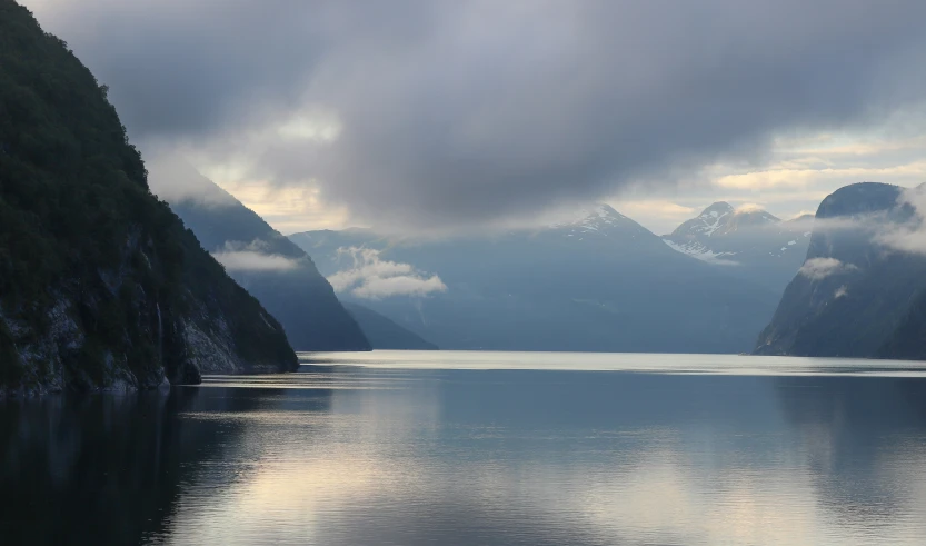 large mountain range looms above the water with low hanging clouds