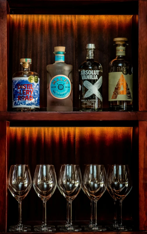 several bottles and glasses sitting on top of a wooden shelf