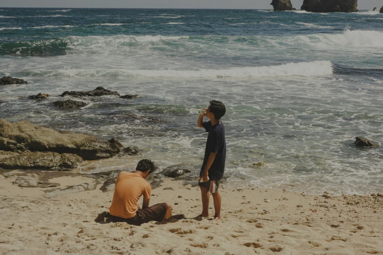 two boys are sitting on the beach while the waves come in