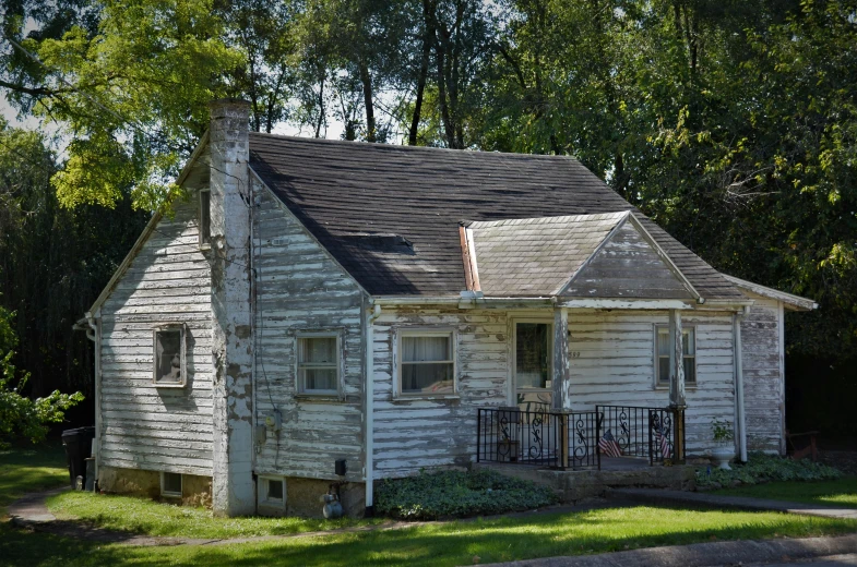 an old white wooden house is sitting in the middle of a yard