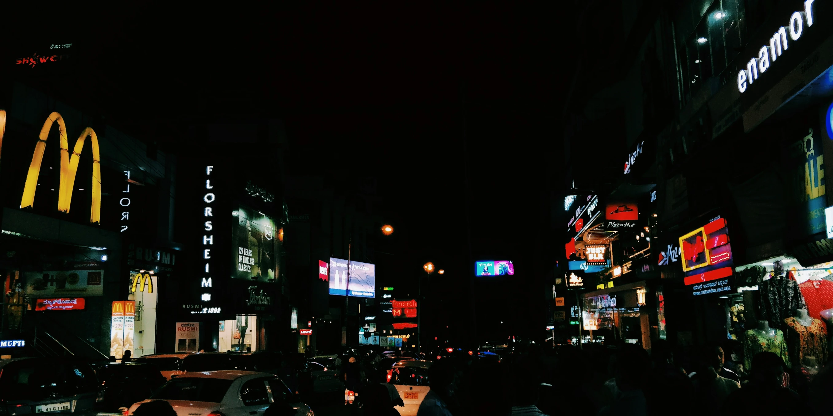 a crowded street with cars, pedestrians and neon signs at night