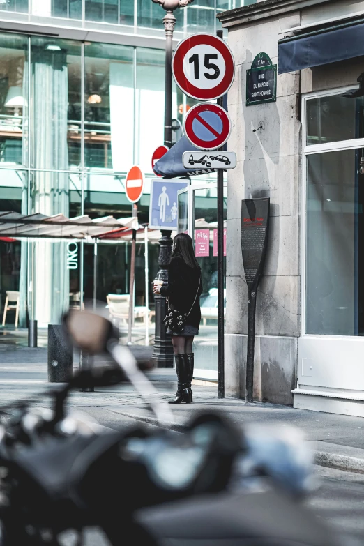 an older woman crossing the street with a lot of road signs on a pole