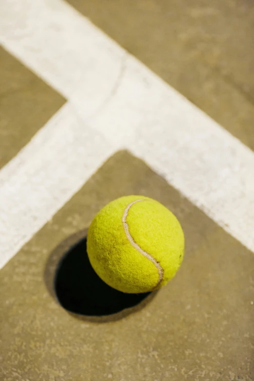 a tennis ball sits on the ground in a shadow