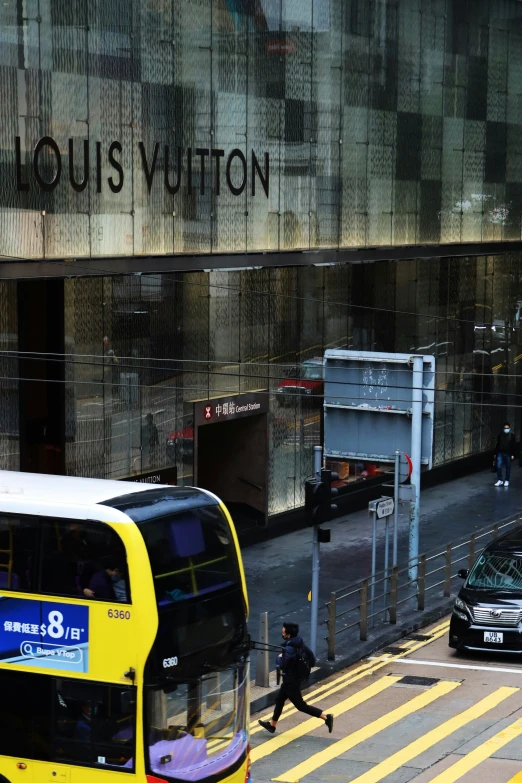 a man crossing the street with a yellow double decker bus