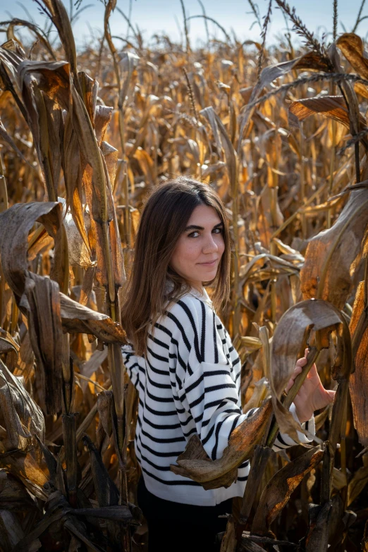 girl in striped shirt standing in cornfield with stalk on face