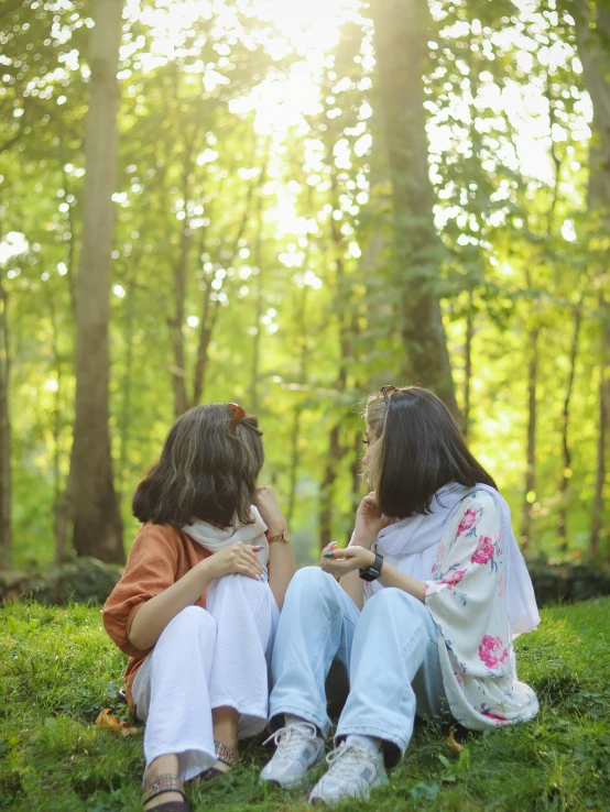 two children, one of them holding her hand in their hands, are sitting on the grass in front of some trees